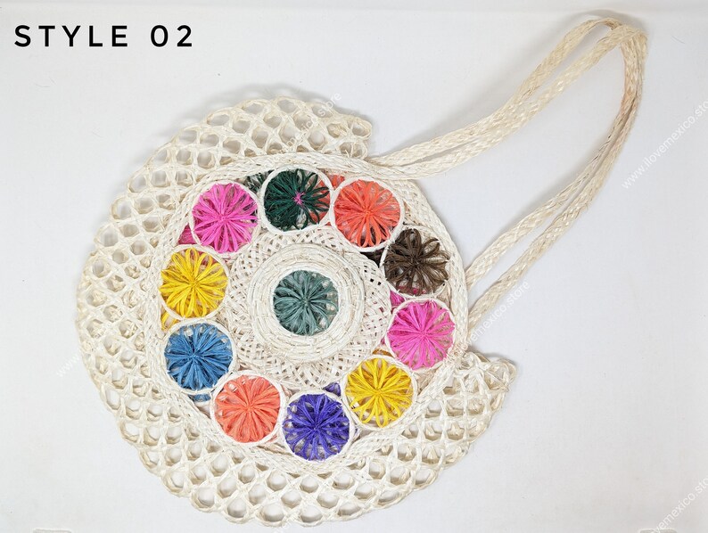 Pu&ograve; includere: Una borsa rotonda intrecciata color bianco sporco con due lunghi manici, che riporta il testo STYLE 02 nell'angolo in alto a sinistra. La borsa presenta un motivo circolare centrale circondato da dieci piccoli accenti intrecciati a forma di stella nei colori rosa, verde, arancione, marrone, giallo, blu e viola.