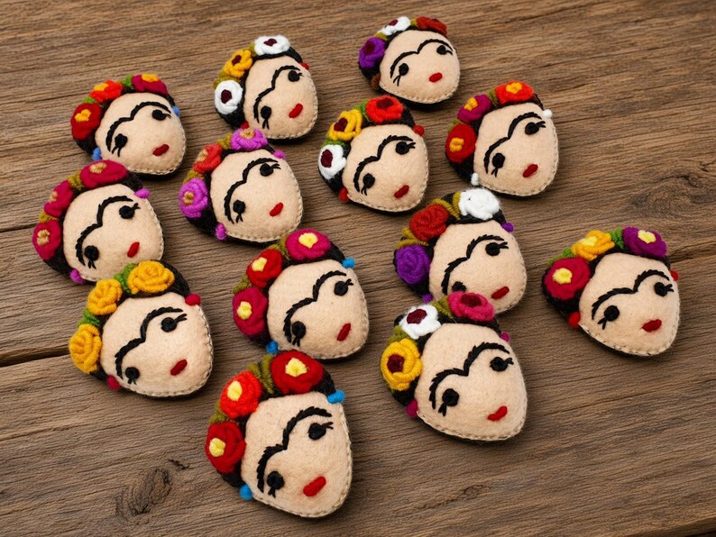 May include: A collection of twelve felted wool appliques, each shaped as a face with dark eyebrows, red lips, and a crown of colorful flowers in shades of red, yellow, purple, and white, arranged on a textured brown wooden surface.