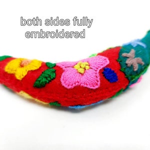 May include: A red felt banana with colourful embroidered flowers on both sides. The banana is a handmade decorative item.