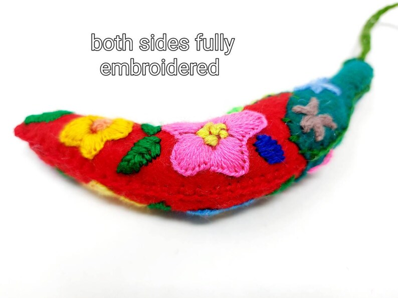 May include: A red felt banana with colourful embroidered flowers on both sides. The banana is a handmade decorative item.