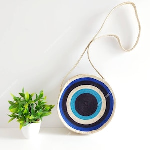 May include: A round, woven bag with a blue, white, and black concentric circle pattern. The bag has a long, woven strap.