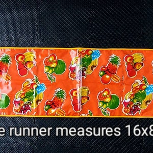 May include: Orange table runner with a yellow border and a repeating pattern of colorful fruit. Each table runner measures 16x80 inches.