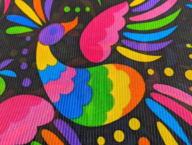 May include: A black mesh fabric featuring a vibrant, multi-colored bird graphic. The bird is composed of bright neon pink, blue, green, yellow, orange, and purple segments. Additional colorful abstract shapes and dots surround the bird design.