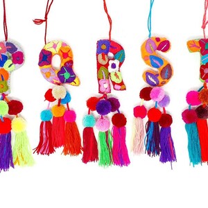 May include: Five colourful felt letters, P, Q, R, S, and T, are embroidered with floral patterns and have pom-poms and tassels hanging from the bottom.