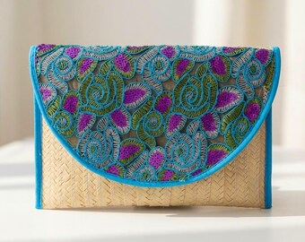 May include: A rectangular envelope clutch bag made of woven tan straw. The flap features an intricate overlay of blue, green, and purple embroidered floral patterns with small purple sequins, finished with a bright blue fabric trim border.