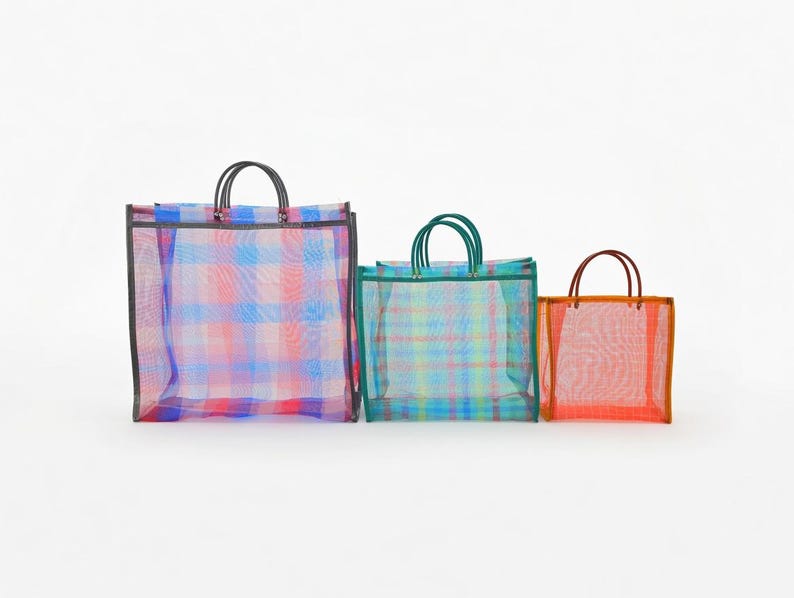 May include: Three rectangular tote bags made of semi-transparent mesh material in varying sizes. The largest bag features a blue and pink plaid pattern with black handles. The medium bag has a teal and yellow plaid pattern with teal handles.