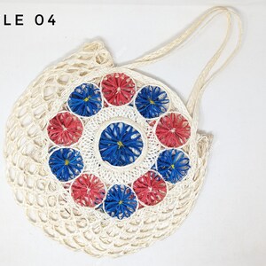 Pu&ograve; includere: Una borsa tote rotonda intrecciata color bianco sporco con due manici, che riporta il testo STYLE 04 nell'angolo in alto a sinistra. Il centro &egrave; decorato con un motivo circolare di fiori intrecciati alternati rossi e blu.