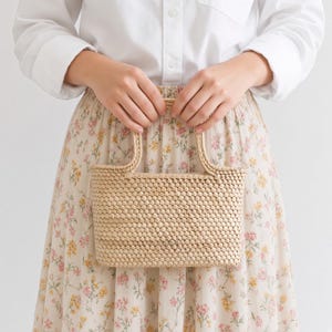 May include: A rectangular woven handbag in a light beige color featuring a tight, uniform basket-weave pattern and two matching woven handles. The bag has a structured, flat-bottomed design with a consistent texture across the entire surface.