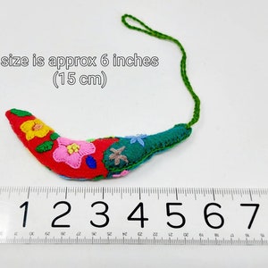 May include: A red, green and yellow embroidered felt chilli pepper ornament with a green string. The ornament is approximately 6 inches (15 cm) long.