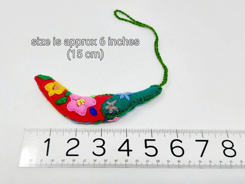 May include: A red, green and yellow embroidered felt chilli pepper ornament with a green string. The ornament is approximately 6 inches (15 cm) long.