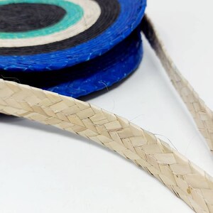 May include: A woven straw bag with a blue, black, and white striped pattern. The bag has a woven straw strap.
