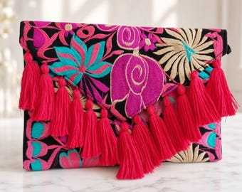 Può includere: Una pochette nera a busta caratterizzata da vivaci ricami floreali nei toni del magenta, turchese e crema. La patta anteriore è decorata con una fila di lunghe nappe rosa acceso che pendono lungo il centro della borsa.