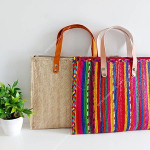 May include: Two woven tote bags with leather handles. One bag is natural colored with a woven texture. The other bag has a colorful striped pattern with red, yellow, green, blue, and pink stripes.