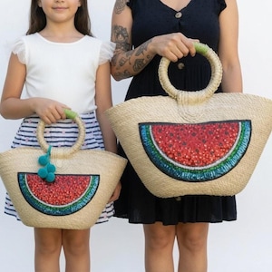 May include: Two straw tote bags with round handles, each featuring a large, semi-circular watermelon graphic on the front. The watermelon design is rendered in red, white, and green sequins. The smaller bag includes a teal pom-pom charm.