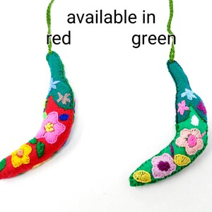 May include: Two felt banana ornaments, one red and one green, with embroidered flowers. The text "available in red green" is written above the ornaments.