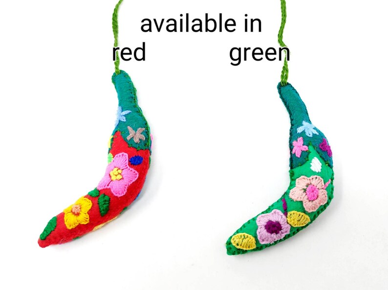 May include: Two felt banana ornaments, one red and one green, with embroidered flowers. The text "available in red green" is written above the ornaments.