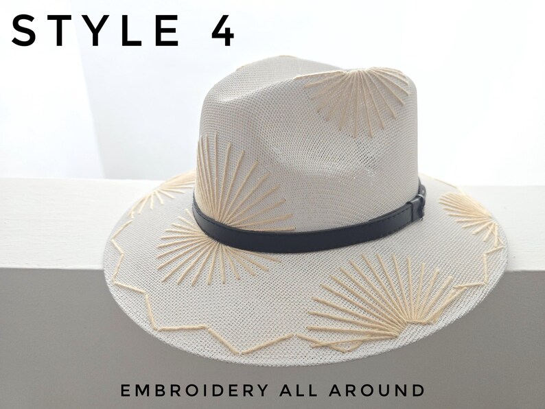 May include: A cream-colored straw fedora hat featuring beige sunburst embroidery patterns on the crown and brim, accented by a thin black band. The text STYLE 4 and EMBROIDERY ALL AROUND is visible in the image, which displays a structured design.