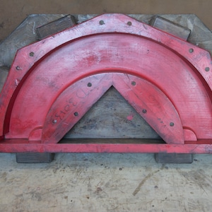 May include: A red wooden mold with a semi-circular shape and a triangular opening in the center. The mold has a number "3313" written on it.