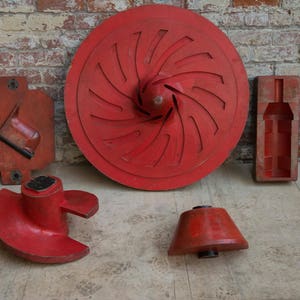 以下が含まれることがあります： 異なる形を鋳造するための赤い木製の型が5つあります。型は木製の表面の上にあります。型は、ボトル、プロペラ、丸い円盤、その他の2つの形を鋳造するためです。