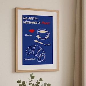 Könnte beinhalten: Gerahmtes Poster mit blauem Hintergrund, weißen Strichzeichnungen eines Croissants, einer Kaffeetasse und eines Löffels, mit dem Text "LE PETIT-DÉJEUNER À PARIS". Eine Vase mit Grün steht auf einem Holztisch.
