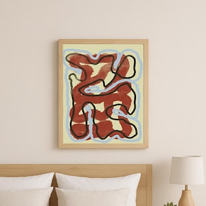 Könnte beinhalten: Abstrakter Kunstdruck in einem Holzrahmen. Das Kunstwerk zeigt ein rotes und schwarzes Design auf hellgelbem Hintergrund mit blauen Akzenten. Die gerahmte Kunst hängt über einem Bett mit weißer Bettwäsche und beigen Kissen.