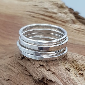 May include: Five silver hammered stacking rings. The rings are stacked on top of each other and are on a wooden surface.