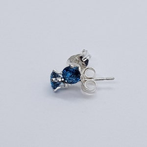 May include: A silver earring with a blue gemstone. The earring has a post and a butterfly back.
