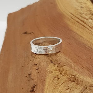 May include: A silver hammered band ring. The ring is wide and has a textured surface.