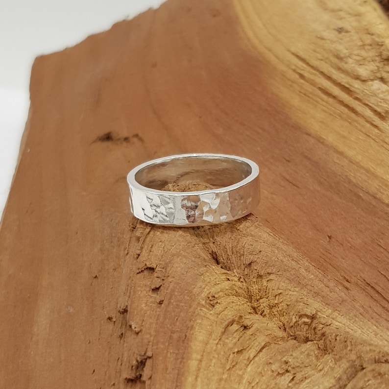 May include: A silver hammered band ring. The ring is wide and has a textured surface.