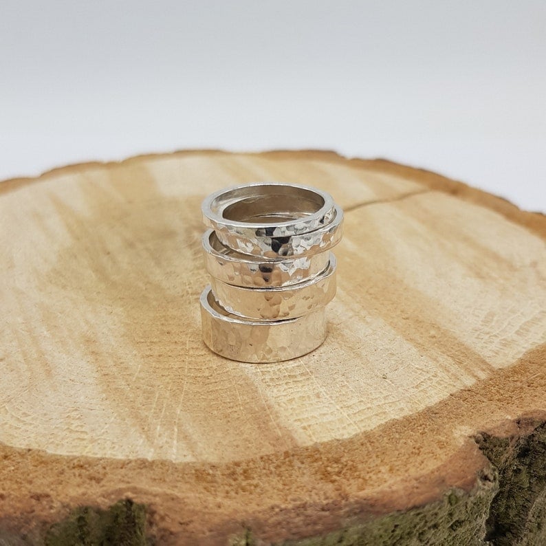 May include: A stack of five silver hammered rings on a wooden surface.