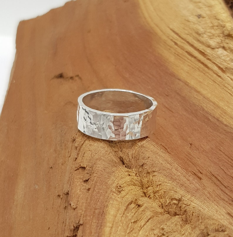 May include: A silver hammered band ring. The ring is wide and has a textured surface.