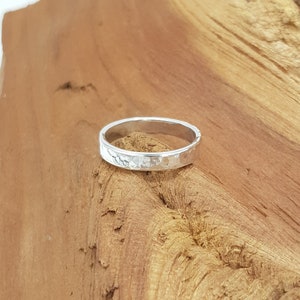 May include: A silver hammered band ring. The ring is simple and has a textured surface.