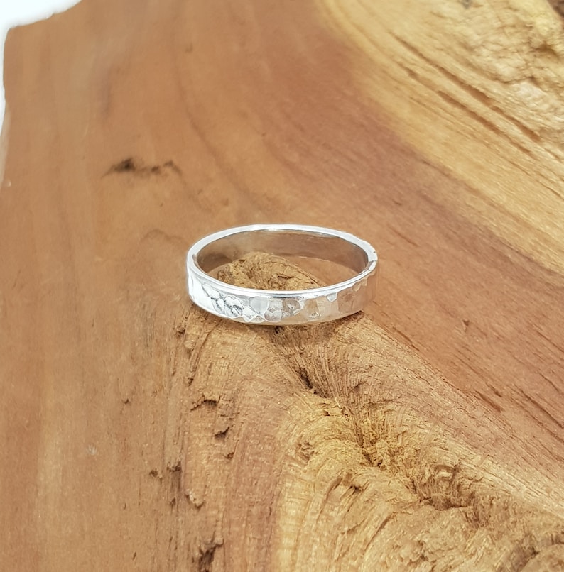 May include: A silver hammered band ring. The ring is simple and has a textured surface.