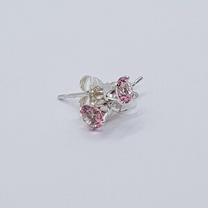 May include: A pair of silver stud earrings with pink gemstones. The earrings are set in a simple, classic style.