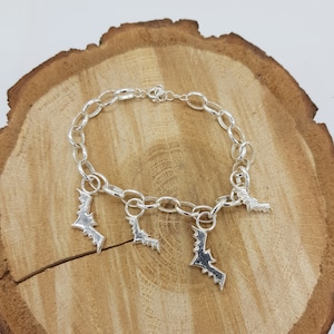 Op de afbeelding: Zilveren armband met vier vleermuis bedels. De armband ligt op een houten oppervlak.