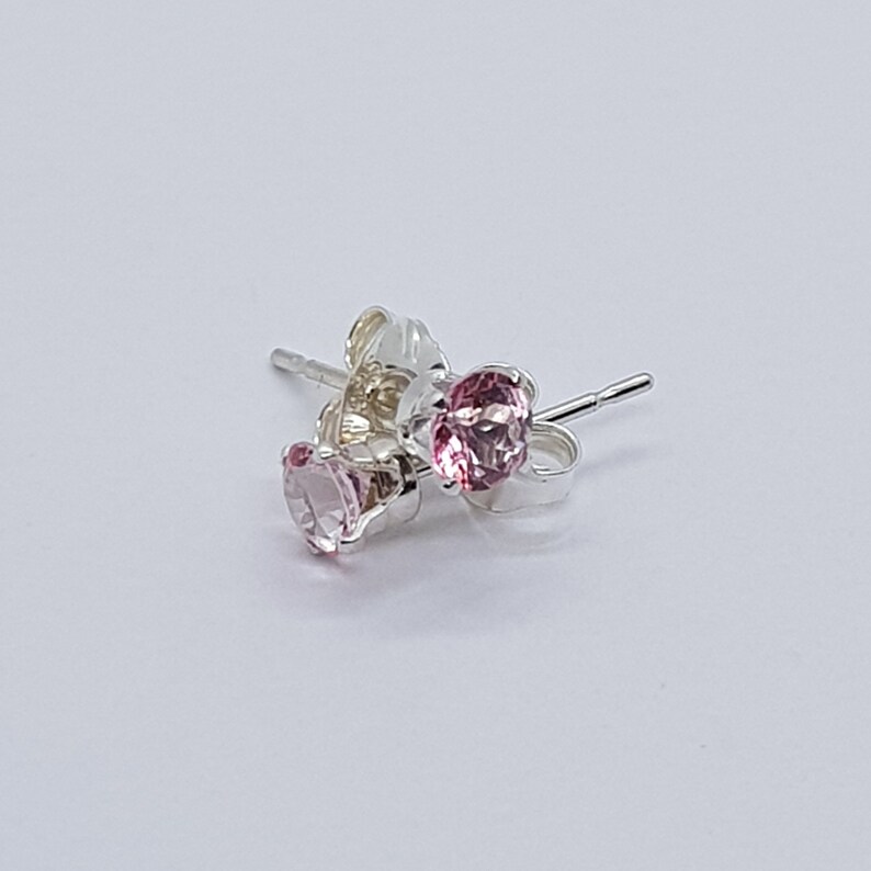 May include: A pair of silver stud earrings with pink gemstones. The earrings are shown on a white background.