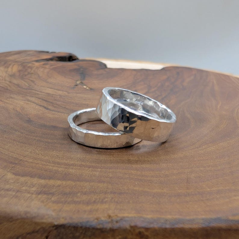 Pu&ograve; includere: Due anelli d'argento con una texture martellata. Gli anelli sono esposti su una superficie di legno. Gli anelli hanno un aspetto strutturato e sfaccettato, che riflette la luce. Gli anelli sono probabilmente in argento sterling o metallo simile.