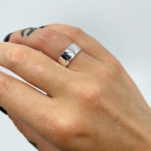 May include: A silver hammered band ring worn on a finger.