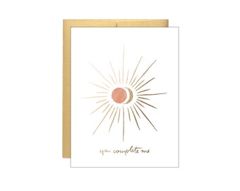 Peut inclure: Une carte blanche avec un motif de soleil et de lune dorés et le texte "you complete me".