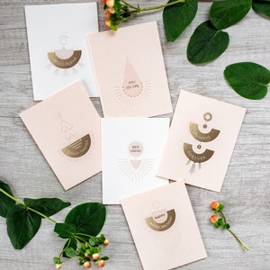 May include: Set of six pink greeting cards with gold foil accents. Each card features a different geometric design and a short message. The messages include "Hello Friend", "You Go Girl", "Many Thanks", "Best Wishes", "Always Forever", and "Happy Birthday".