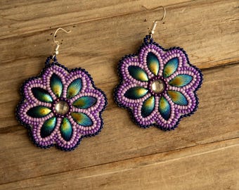 May include: A pair of flower-shaped dangle earrings featuring intricate beadwork. The petals are crafted with iridescent blue and green beads, outlined in purple beads, with a clear central stone and silver-toned metal earring hooks.