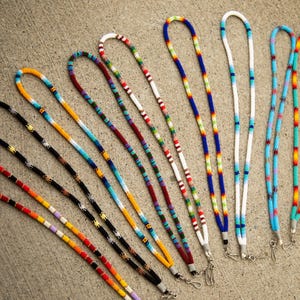 May include: A collection of beaded lanyards in various colors, including black, orange, yellow, blue, and white. Each lanyard features a unique pattern of small, colorful beads and a metal clasp.