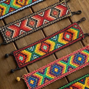 May include: Five wide bracelets crafted from small, colorful glass beads arranged in intricate geometric patterns. Each bracelet features a unique combination of vibrant hues including red, yellow, blue, green, and orange, finished with small beaded loops.