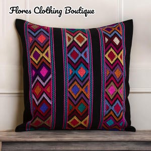 May include: Black pillow with colorful geometric embroidery. The embroidery features a repeating pattern of diamonds and triangles in shades of pink, purple, blue, green, orange, and yellow.