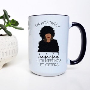 Puede incluir: Taza de caf&eacute; de cer&aacute;mica blanca con borde y asa negros. La taza presenta una ilustraci&oacute;n en blanco y negro de una mujer con una cita que dice "Estoy positivamente endemoniada con las reuniones, etc."