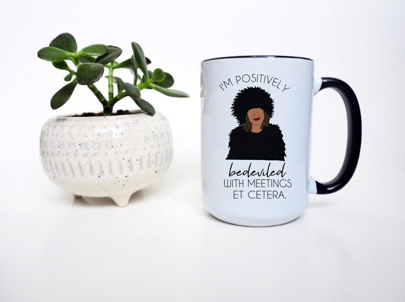Puede incluir: Taza de caf&eacute; de cer&aacute;mica blanca con borde y asa negros. La taza presenta una ilustraci&oacute;n en blanco y negro de una mujer con una cita que dice "Estoy positivamente endemoniada con las reuniones, etc."