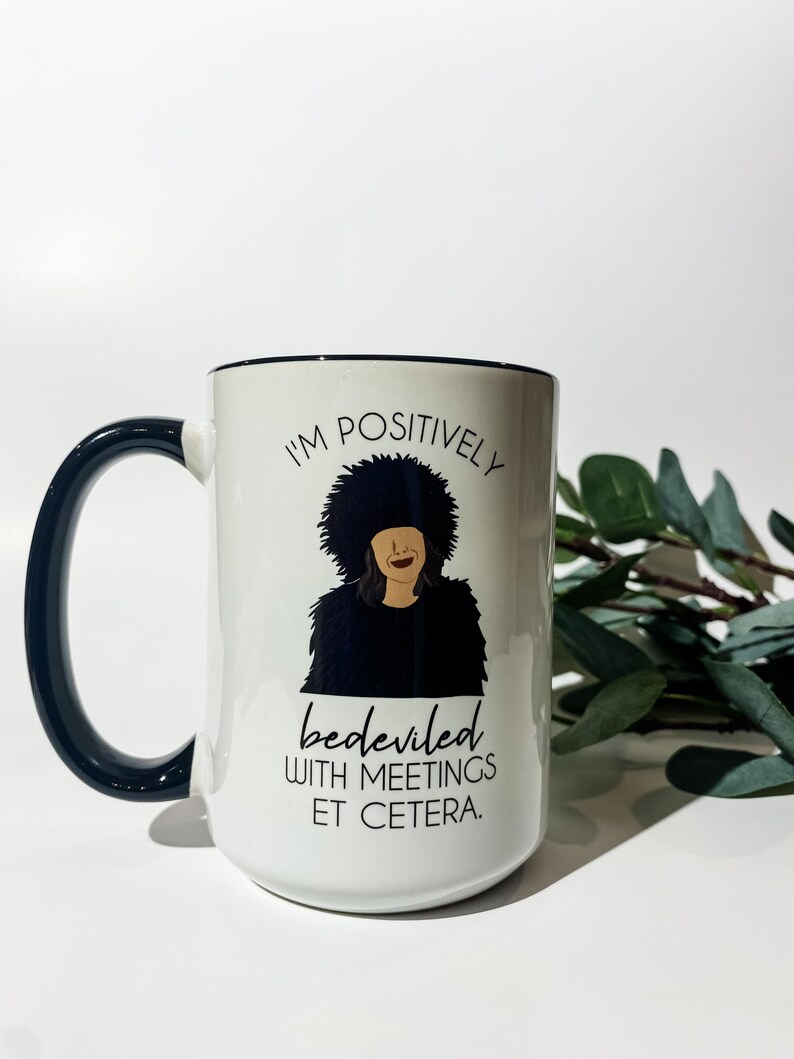 Puede incluir: Taza de cer&aacute;mica blanca con asa y borde negros. La taza presenta una ilustraci&oacute;n en blanco y negro de una persona con una cita que dice "Estoy positivamente atormentado con reuniones etc."