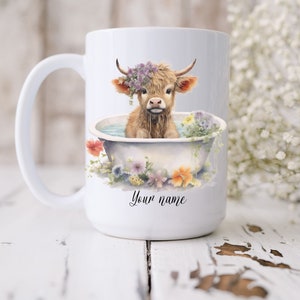 May include: White ceramic mug with a brown and white highland cow wearing a flower crown in a white bathtub with flowers. The text "Your name" is printed on the mug.
