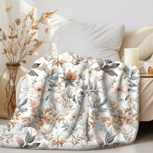 May include: A soft, white blanket with a floral pattern in muted tones of brown, beige, and blue. The blanket is draped over a chair, showcasing the detailed botanical design. The cozy throw blanket adds a touch of nature-inspired elegance to any living space.