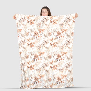 May include: A white fleece blanket with a repeating pattern of brown and orange watercolor leaves.